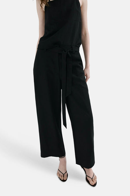 Pantalon noir de MANGO, taille haute ceinturé à coupe large, porté avec un débardeur et des sandales.