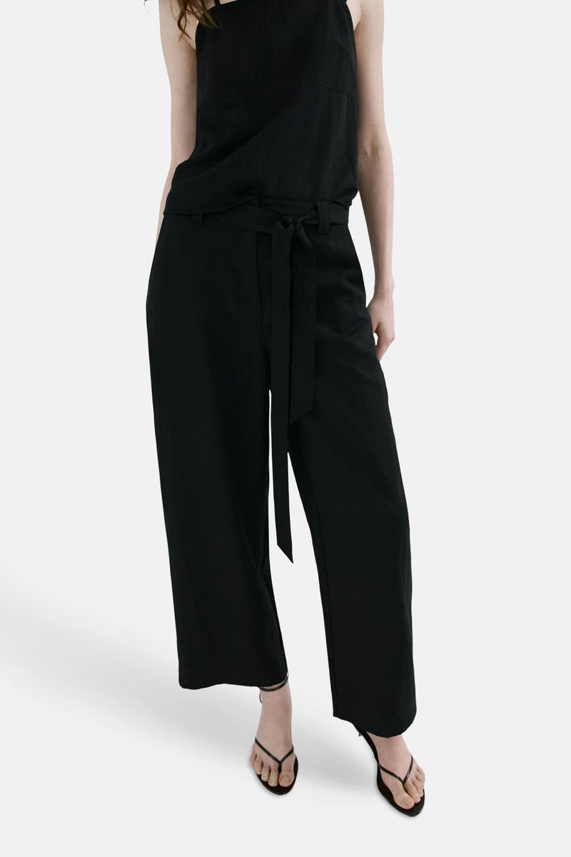 Pantalon noir de MANGO, taille haute ceinturé à coupe large, porté avec un débardeur et des sandales.