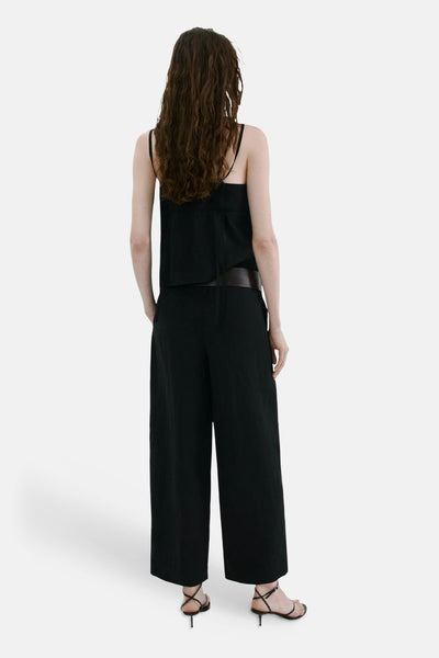 Pantalon noir de MANGO, coupe large et fluide, porté de dos avec un top noir et des sandales à talons.