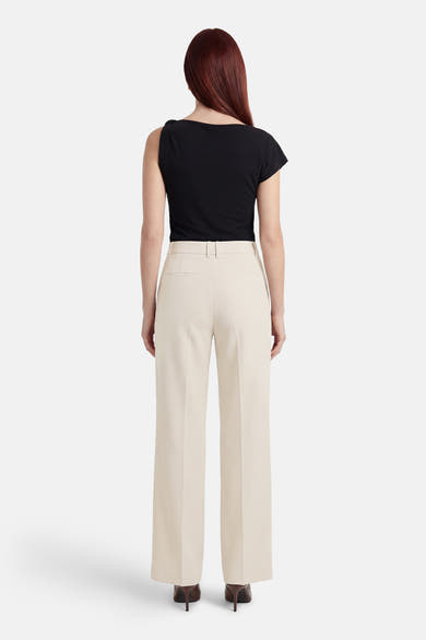 Beige kostuumbroek van MANGO, met een rechte pasvorm, gedragen met een zwarte top en bruine pumps.