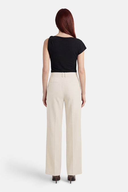Pantalon de costume beige de MANGO, avec une coupe droite, porté avec un haut noir et des escarpins marron.