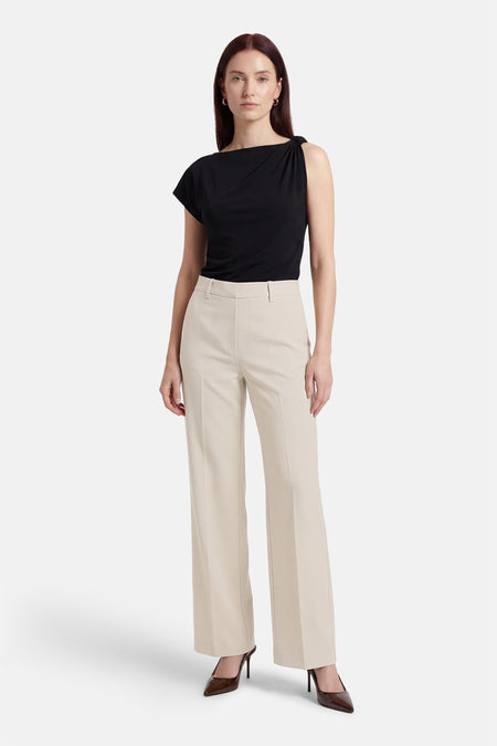 Pantalon de costume beige de MANGO, coupe droite tombant sur des escarpins marron.