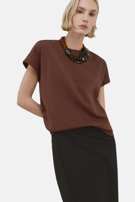 Top sans manches brun de MANGO, porté avec une jupe noire et un collier à grosses pierres.