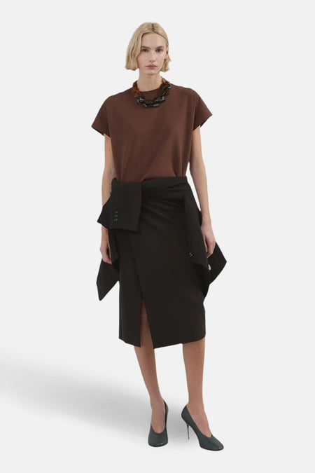 Top sans manches brun par MANGO, porté avec une jupe noire portefeuille et un collier à grosses pierres.