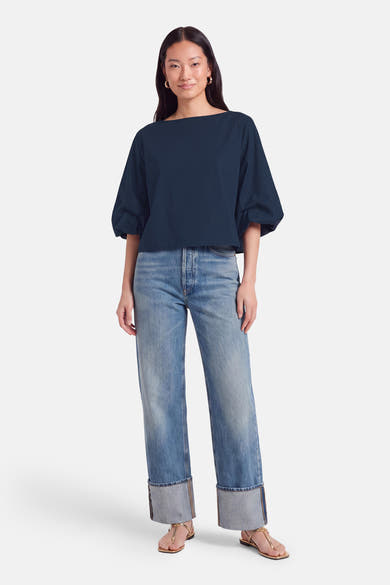 Blouse bleue à manches courtes par Terra di Siena, coupe ample, col bateau, portée avec jeans délavés et sandales dorées, vue de face.