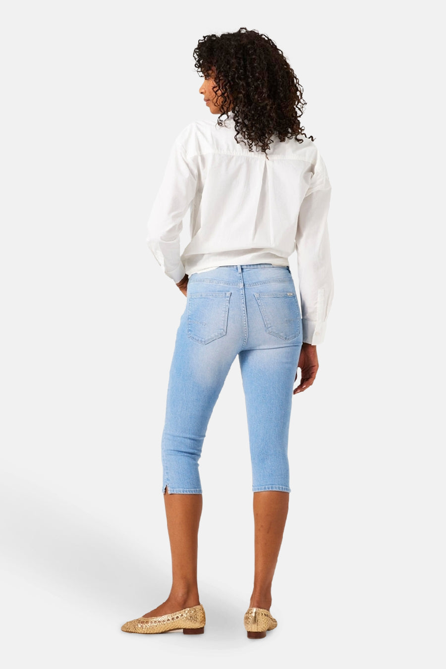 Jean denim bleu clair de GARCIA, porté avec une chemise blanche à manches longues et des chaussures dorées.
