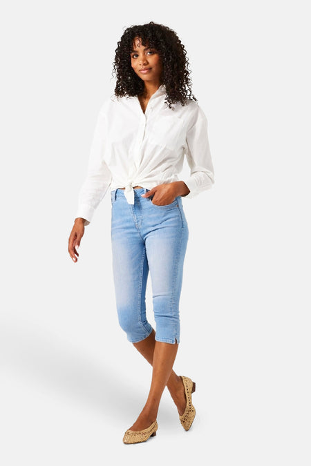 Jean en denim bleu clair de GARCIA, porté avec une chemise blanche nouée et des chaussures plates tressées.
