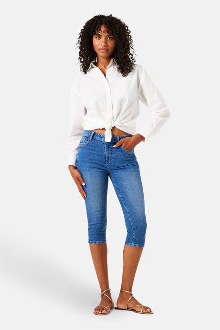 Jean bleu denim mi-long de GARCIA, porté avec une chemise blanche nouée et des sandales dorées.
