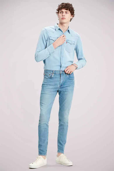 Slim-fit spijkerbroek in lichtblauw denim van Levi's, gedragen met een overhemd en witte schoenen.