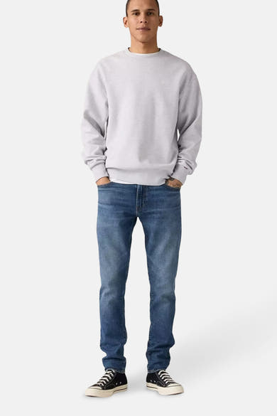 Middelblauwe Levi's® tapered jeans, gedragen met een grijs sweatshirt en zwarte sneakers.