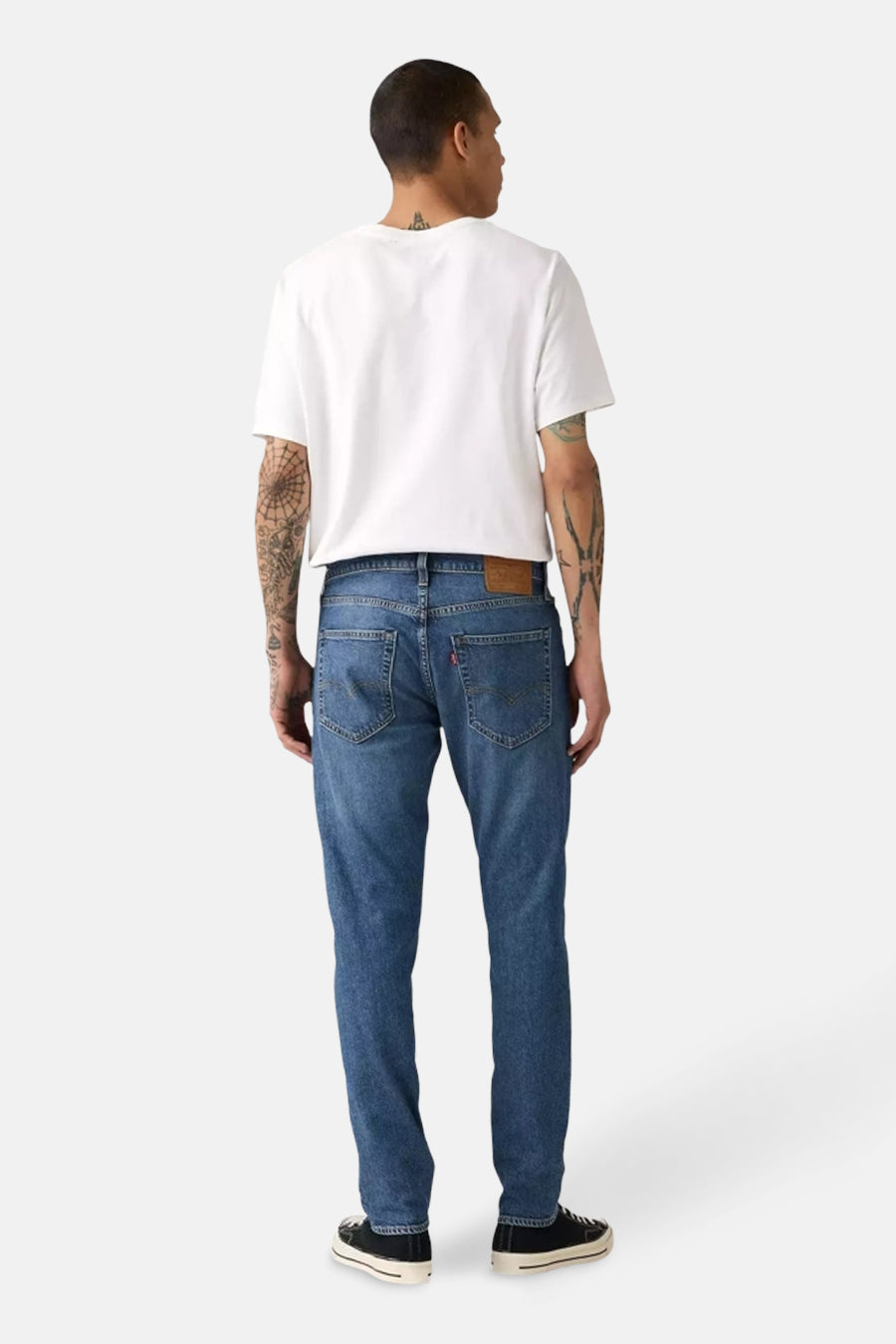 Taps toelopende spijkerbroek in middinblauw denim van Levi's, gedragen met een wit T-shirt en zwarte sneakers, achtergezicht.