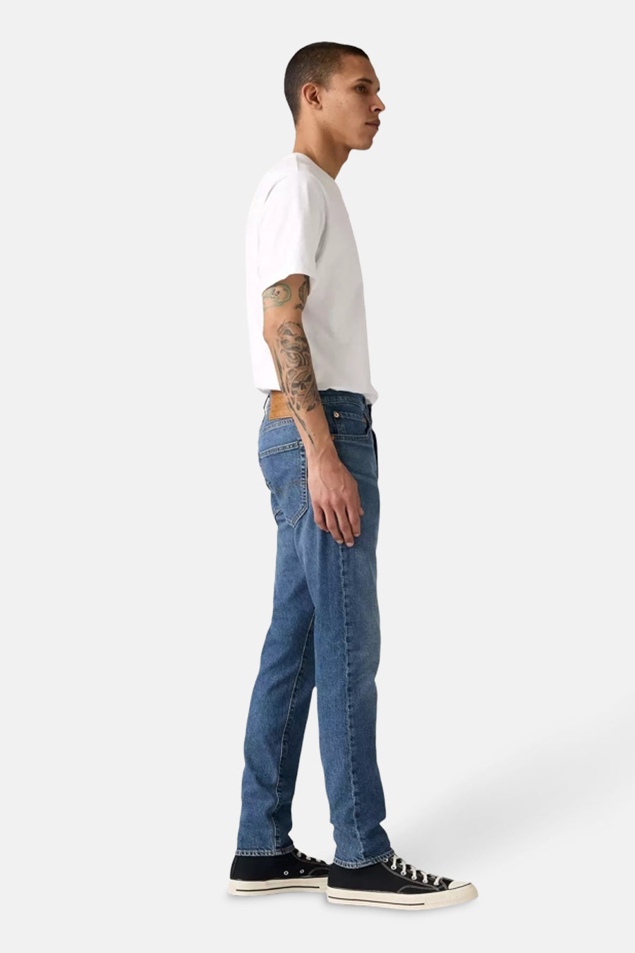 Middelblauwe, taps toelopende jeans van Levi's, gedragen met een wit T-shirt en zwarte sneakers, zijwaarts gezien.
