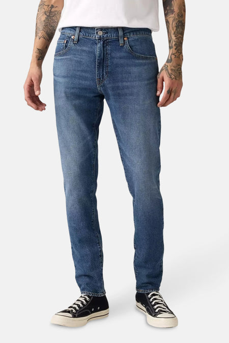 Jean tapered en denim bleu moyen de Levi's®, porté avec des baskets montantes noires à lacets blancs.

