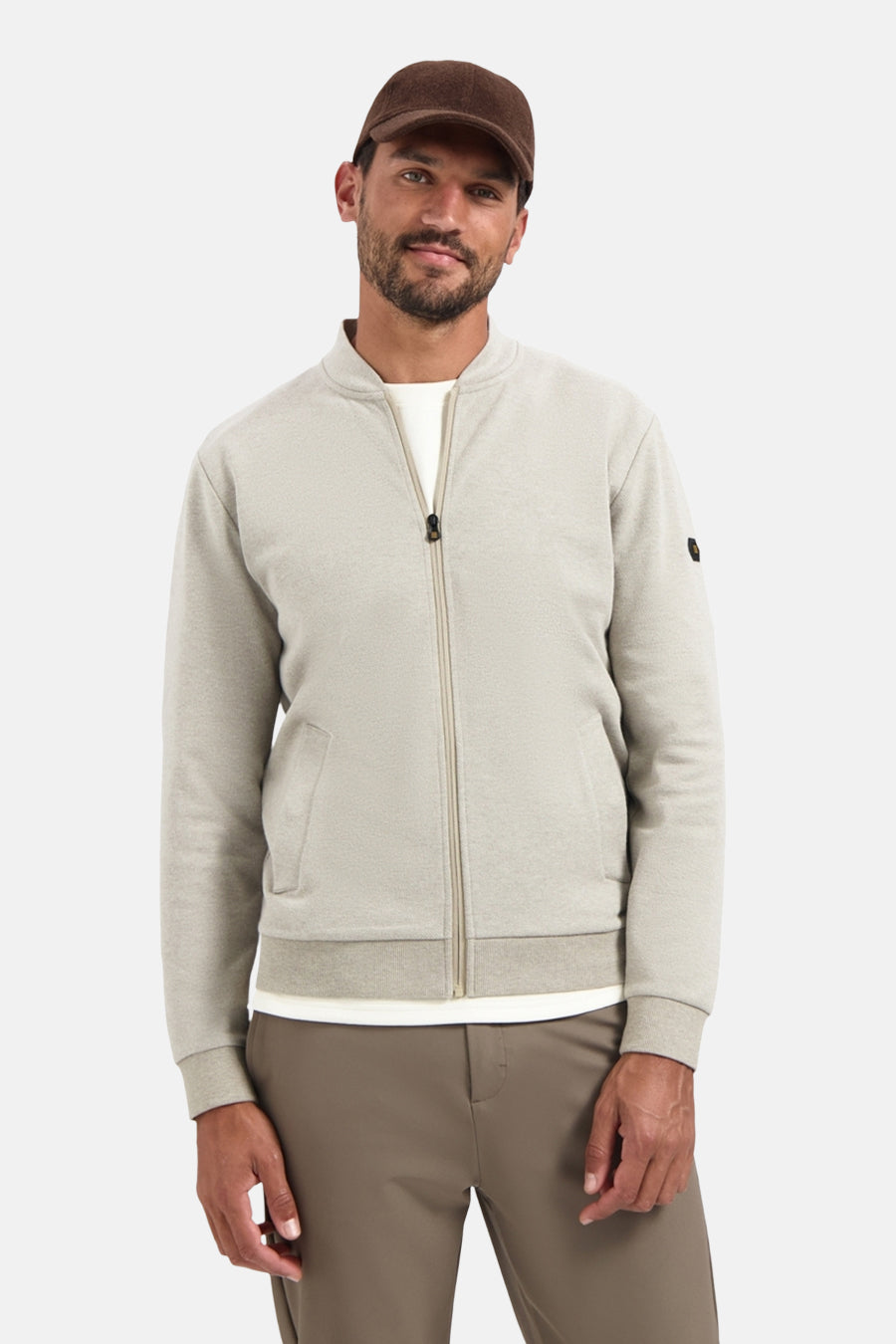 Beige gilet van NO EXCESS, met ritssluiting, gedragen over een wit T-shirt en een bruine broek, met een pet op.