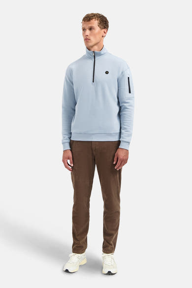 Blauwe coltrui van NO EXCESS, met ritssluiting en een ritszak op de mouw, gedragen met een bruine broek.