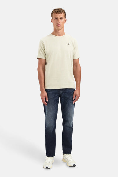 Beige T-shirt met korte mouwen van NO EXCESS, met een klein zwart logo op de borst, gedragen met een spijkerbroek en sneakers.