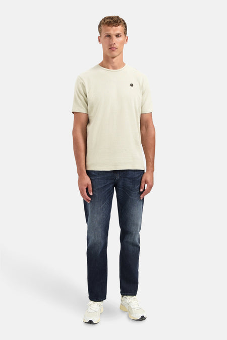 Beige T-shirt met korte mouwen van NO EXCESS, met een klein zwart logo op de borst, gedragen met een spijkerbroek en sneakers.