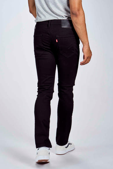 Jean fuselé noir de Levi's, avec étiquette en cuir noir et étiquette rouge, porté avec un t-shirt gris et des chaussures blanches.