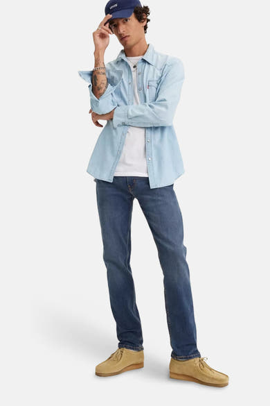 Middelblauwe, taps toelopende jeans van Levi's®, gedragen met een lichtblauw spijkeroverhemd en zandkleurige schoenen.