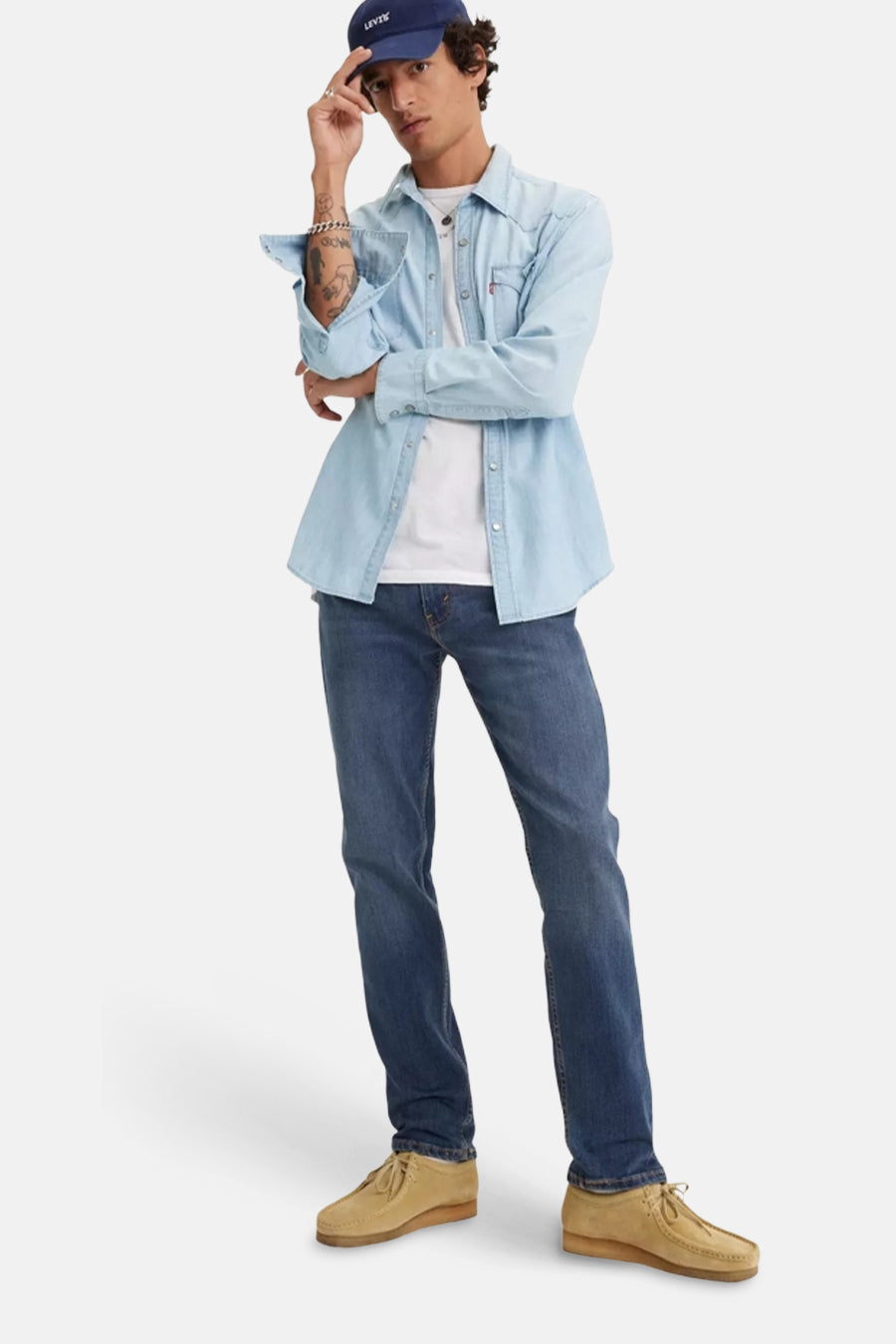 Middelblauwe, taps toelopende jeans van Levi's®, gedragen met een lichtblauw spijkeroverhemd en zandkleurige schoenen.