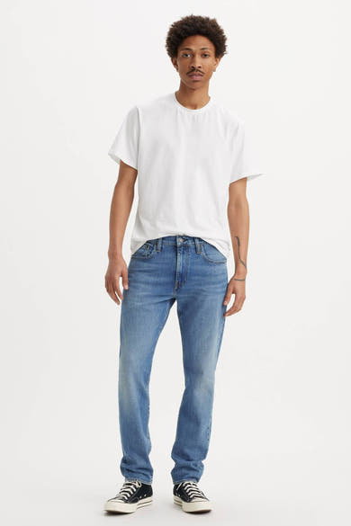 Jean fuselé en denim bleu moyen de Levi's, porté avec un t-shirt blanc et des baskets en toile noires.
