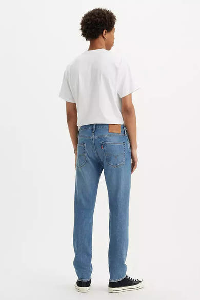 Jean fuselé en denim bleu moyen de Levi's, avec poches arrière et porté avec un t-shirt blanc uni.