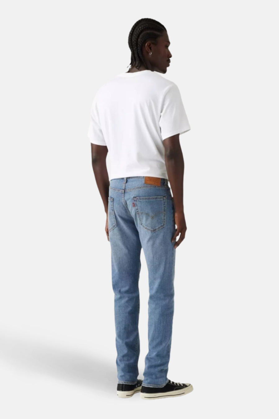 Jeans fuselés en denim bleu clair de Levi's, vus de dos, portés avec un t-shirt blanc uni et des baskets noires.