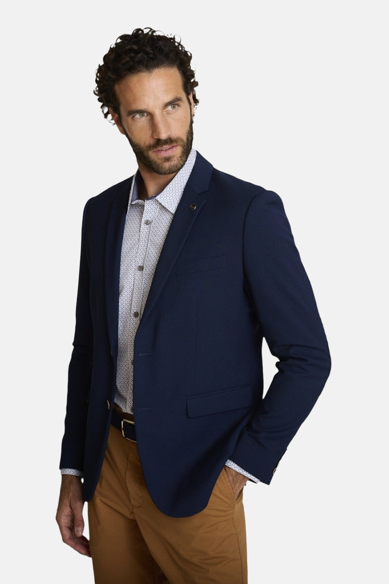 Blazer bleu de DELAHAYE, porté sur une chemise à motifs discrets et un pantalon chino marron.