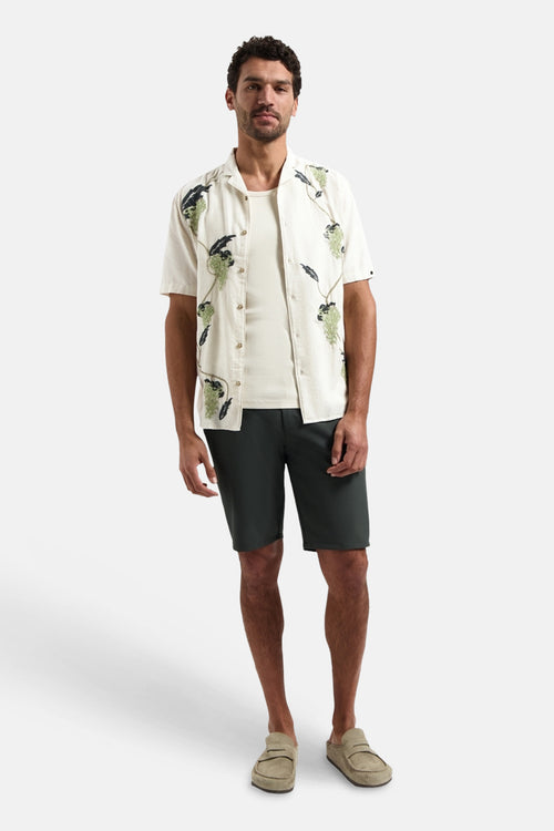 Crèmekleurig overhemd met korte mouwen van NO EXCESS, met groene en donkere patronen, gedragen over een T-shirt met een antracietkleurige korte broek.