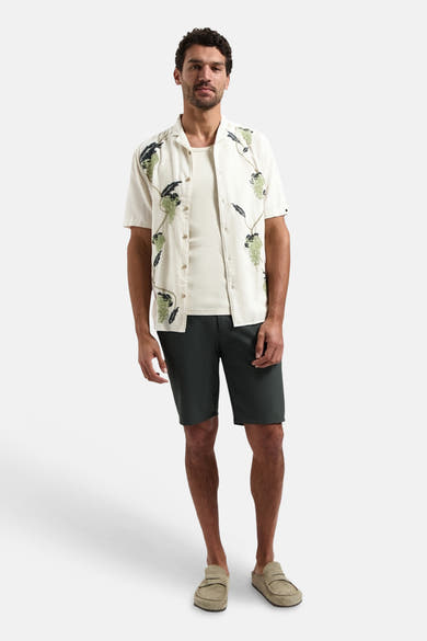 Crèmekleurig overhemd met korte mouwen van NO EXCESS, met groene en donkere patronen, gedragen over een T-shirt met een antracietkleurige korte broek.