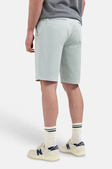 Kort, lichtgroen NO EXCESS canvas rugzak, gedragen op de rug door een man met een T-shirt met patroon en sneakers.