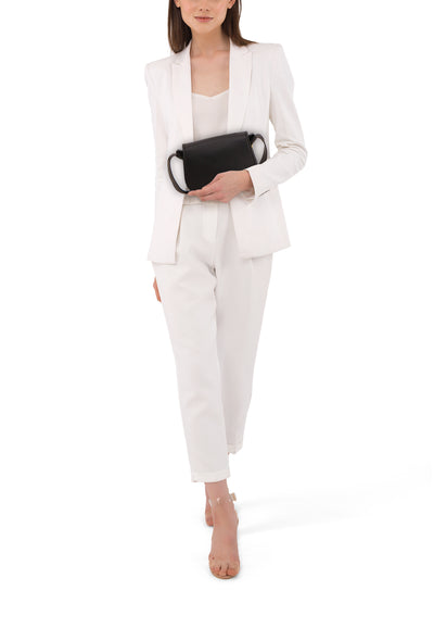 Sac à bandoulière noir de Tamaris, porté avec un tailleur pantalon blanc et des sandales à talons transparents.
