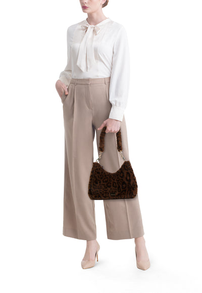 Sac à bandoulière en fourrure marron de Tamaris avec chaîne dorée, porté avec un chemisier et un pantalon beiges.