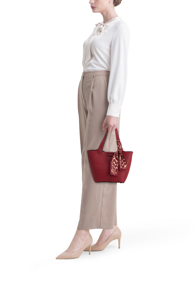 Sac à bandoulière rouge par TAMARIS avec un foulard à motif léopard attaché, porté avec un chemisier blanc et un pantalon beige.