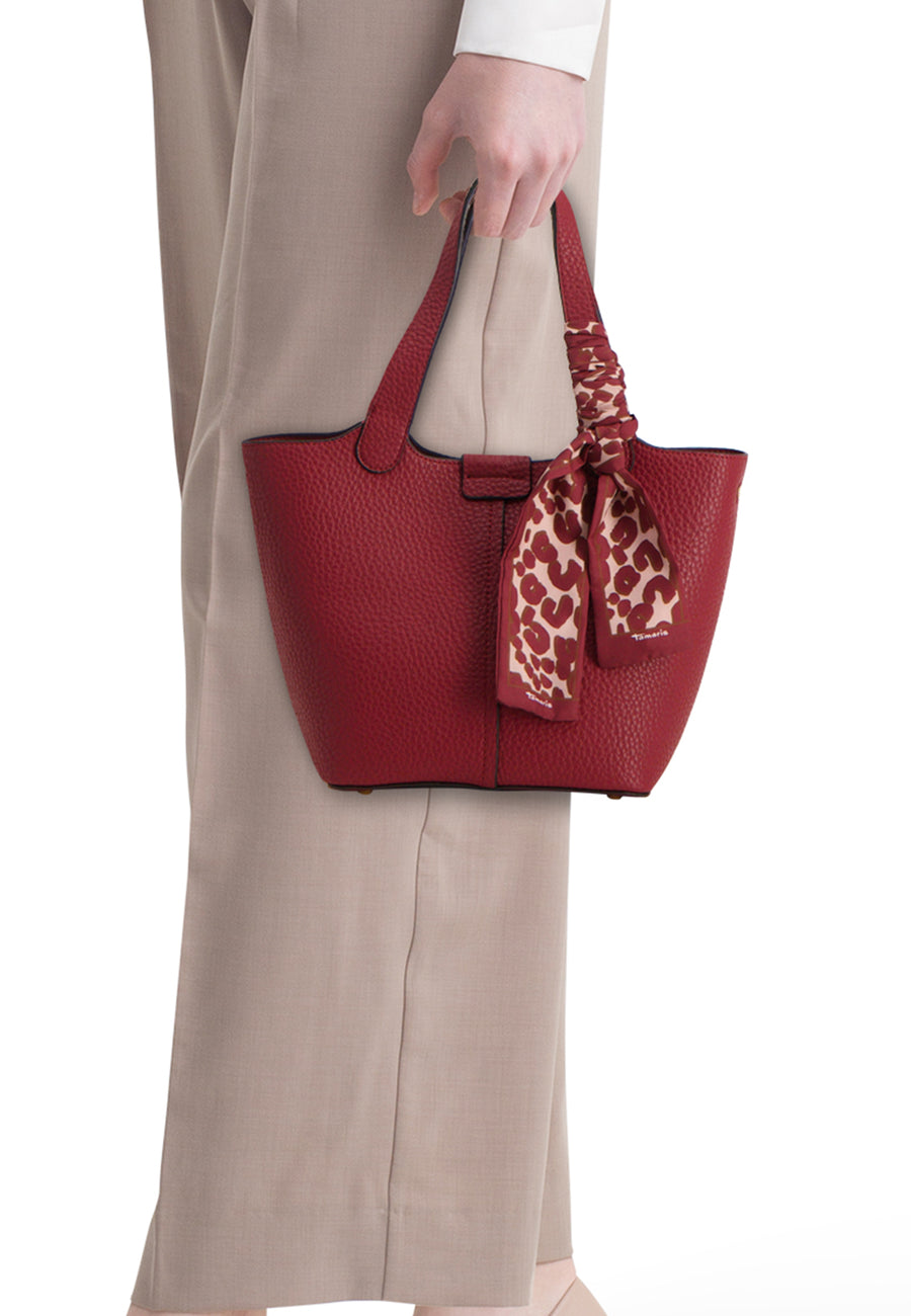 Sac à bandoulière rouge en cuir de TAMARIS, avec foulard à motif animalier noué à la bandoulière, porté avec un pantalon beige.
