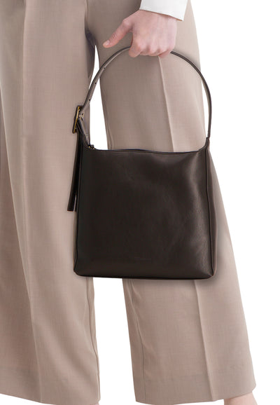 Bruine riemzak TAMARIS, gedragen in de hand met een ronde riem, over een beige broek.