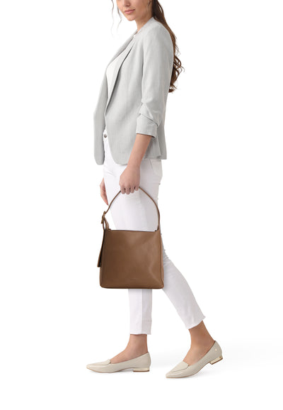 Sac à bandoulière taupe de TAMARIS, porté avec un blazer gris et un pantalon blanc.