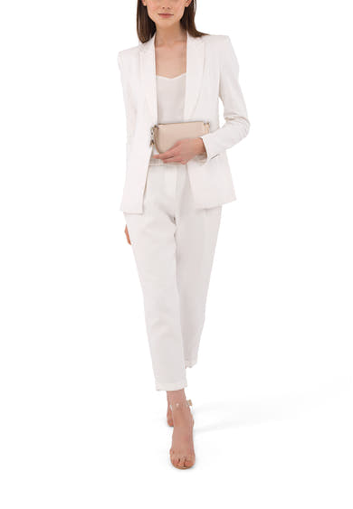 Sac à main beige de TAMARIS, porté avec un tailleur pantalon blanc et des sandales transparentes.