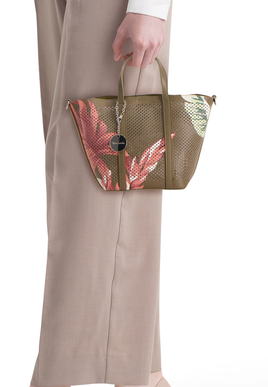 Sac à main kaki de TAMARIS perforé avec imprimé floral rouge et pendentif logo, tenu à la main.