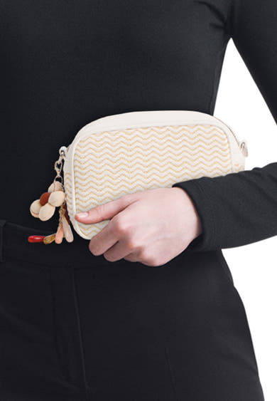 Witte handtas van TAMARIS met chevronpatroon en decoratieve bedel, gedragen met zwarte kleding.