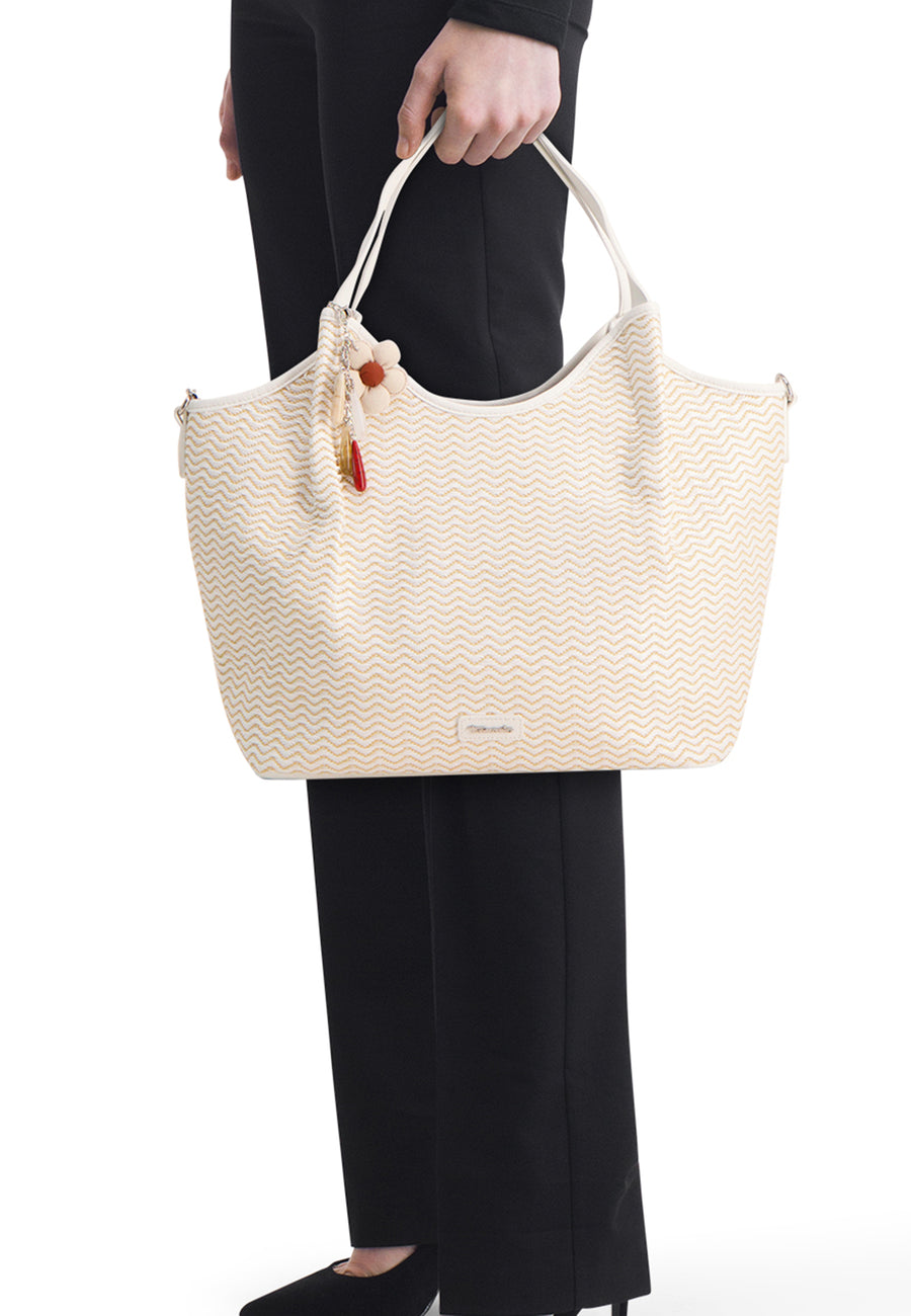 Sac à main blanc par Tamaris, avec motif à chevrons, orné d'une fleur décorative et porté à la main.