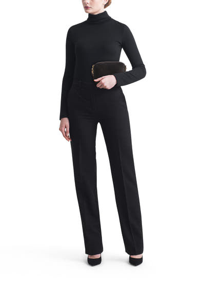 Sac à main noir de TAMARIS, porté avec un pull à col roulé et un pantalon noir, sur fond blanc.