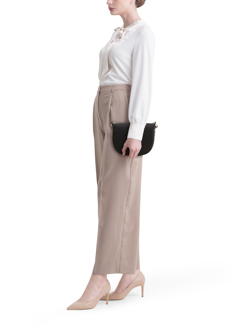 Sac à main noir en cuir, de TAMARIS, porté avec un chemisier blanc et un pantalon beige avec des talons assortis.