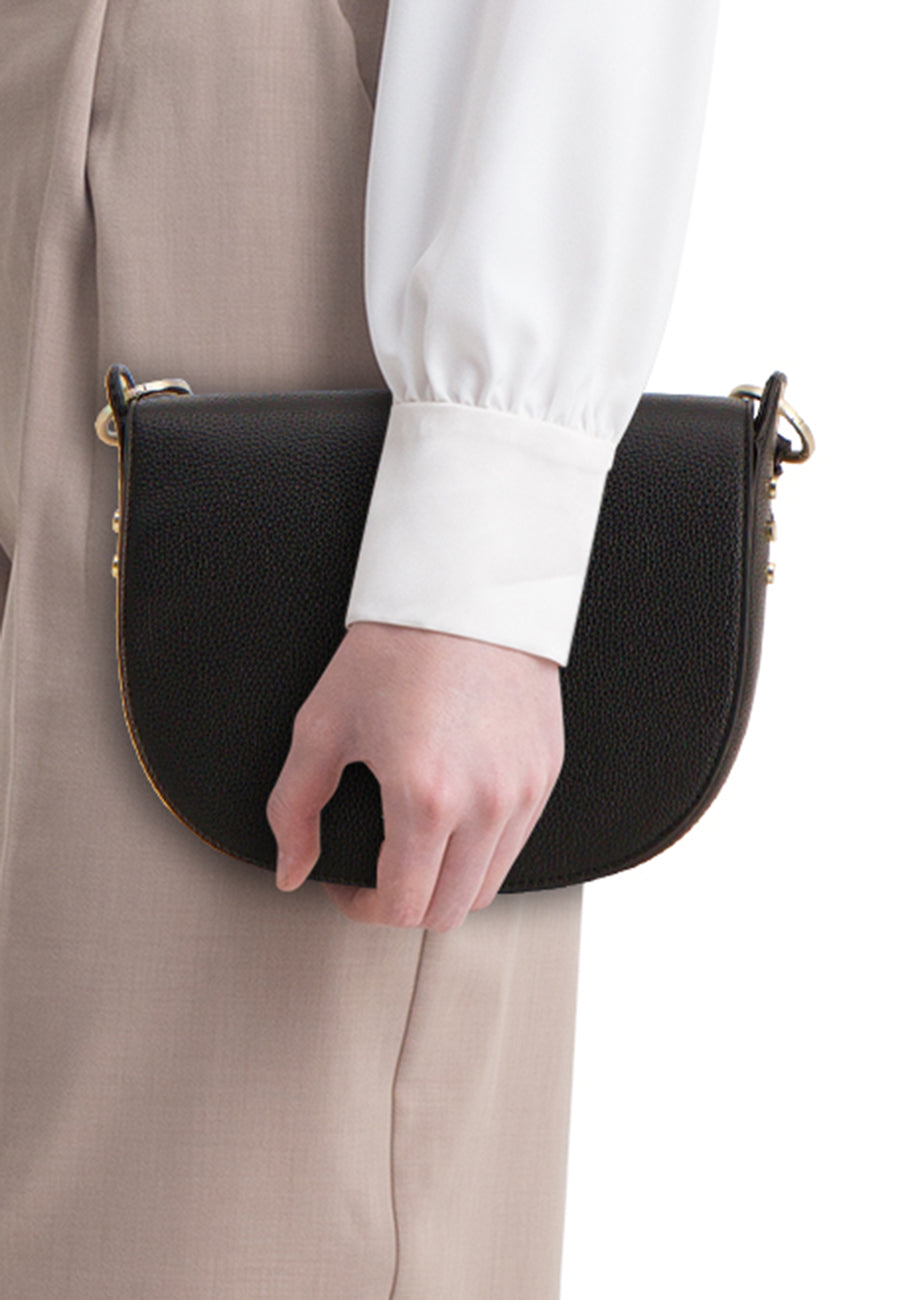 Zwarte handtas van TAMARIS, in de hand gehouden met een wit overhemd en een beige broek.