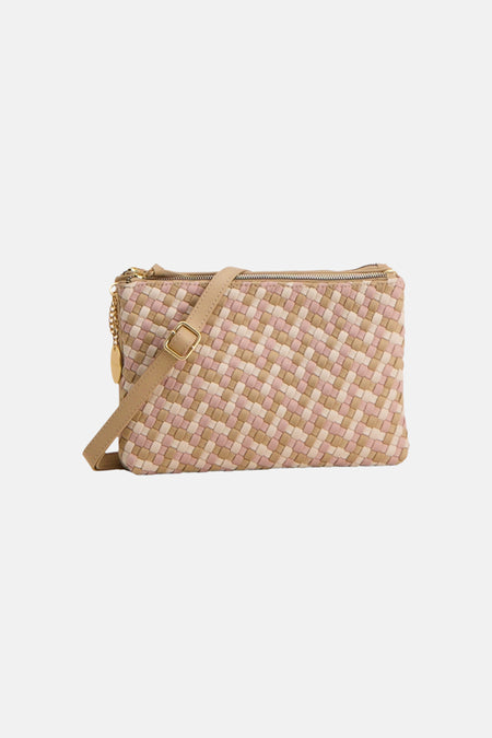 Multikleuren gevlochten handtas van TAMARIS met beige en lichtroze vierkanten, vastgehouden door een persoon in het zwart, zijwaarts gezien.