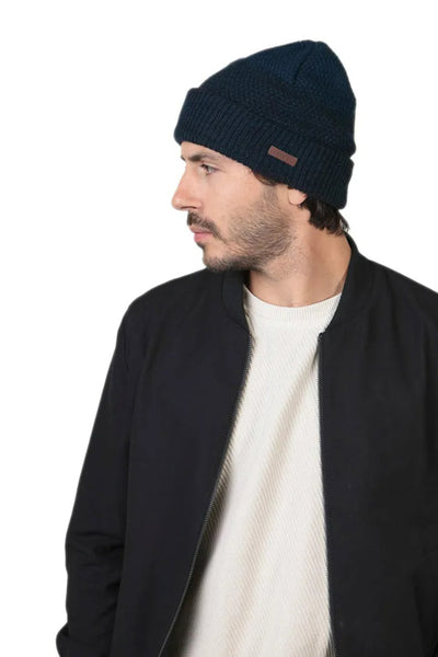 Bonnet bleu de BARTS, en tricot côtelé avec un petit patch en cuir sur le côté, porté avec une veste noire.