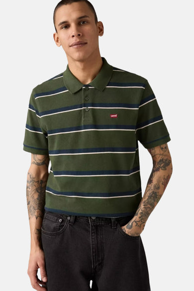 Polo à manches courtes vert rayé de Levi's, porté avec un jean noir et orné de tatouages sur les bras.
