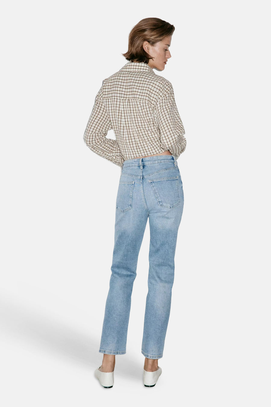 Light blue mom jeans by NEWMOM, back view showing high waist, straight fit, and faded denim texture with white shoes and plaid shirt.