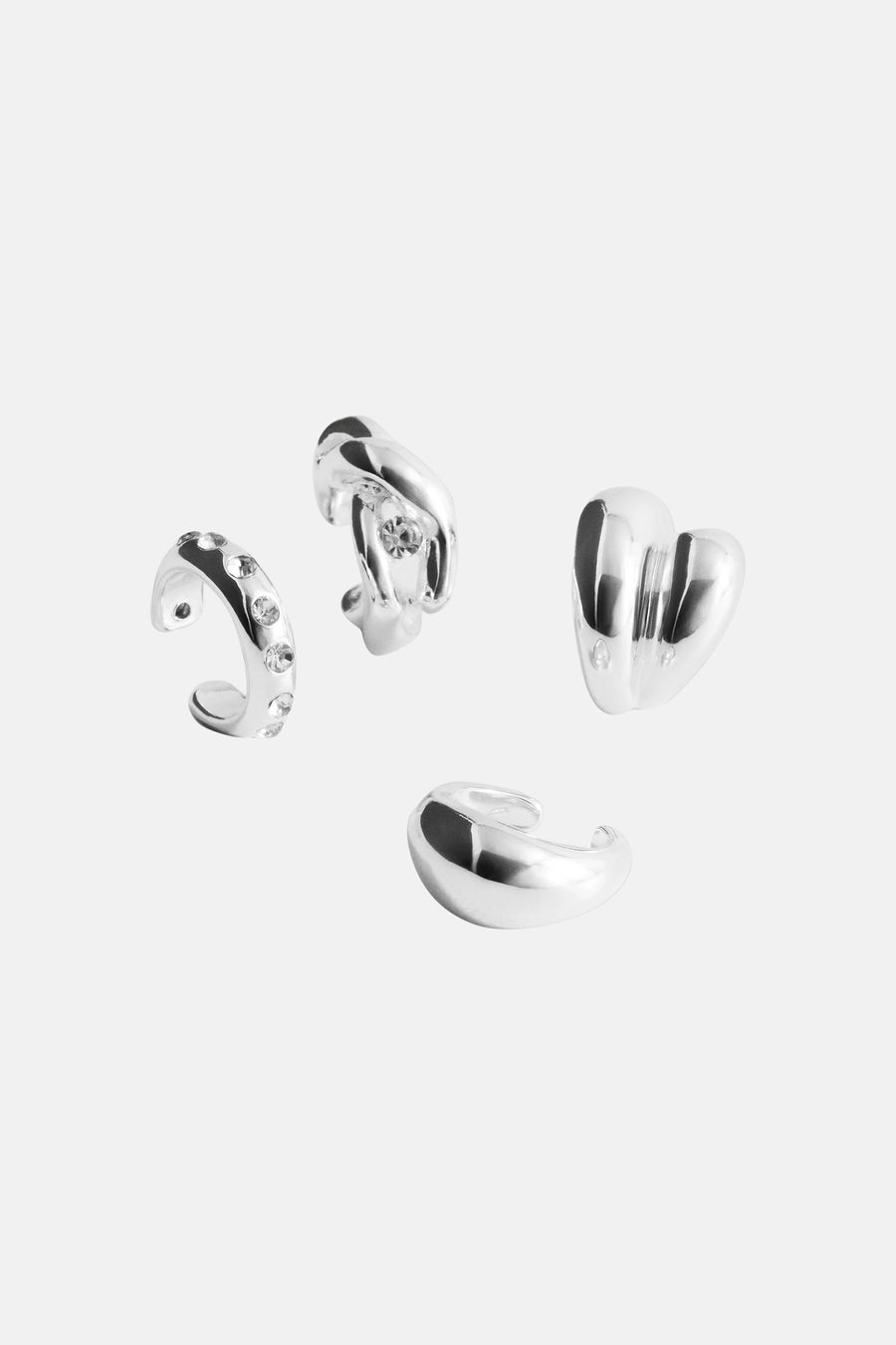 Silver heart-shaped and curved hoop earrings with clear crystal accents, displayed in a scattered arrangement on white background