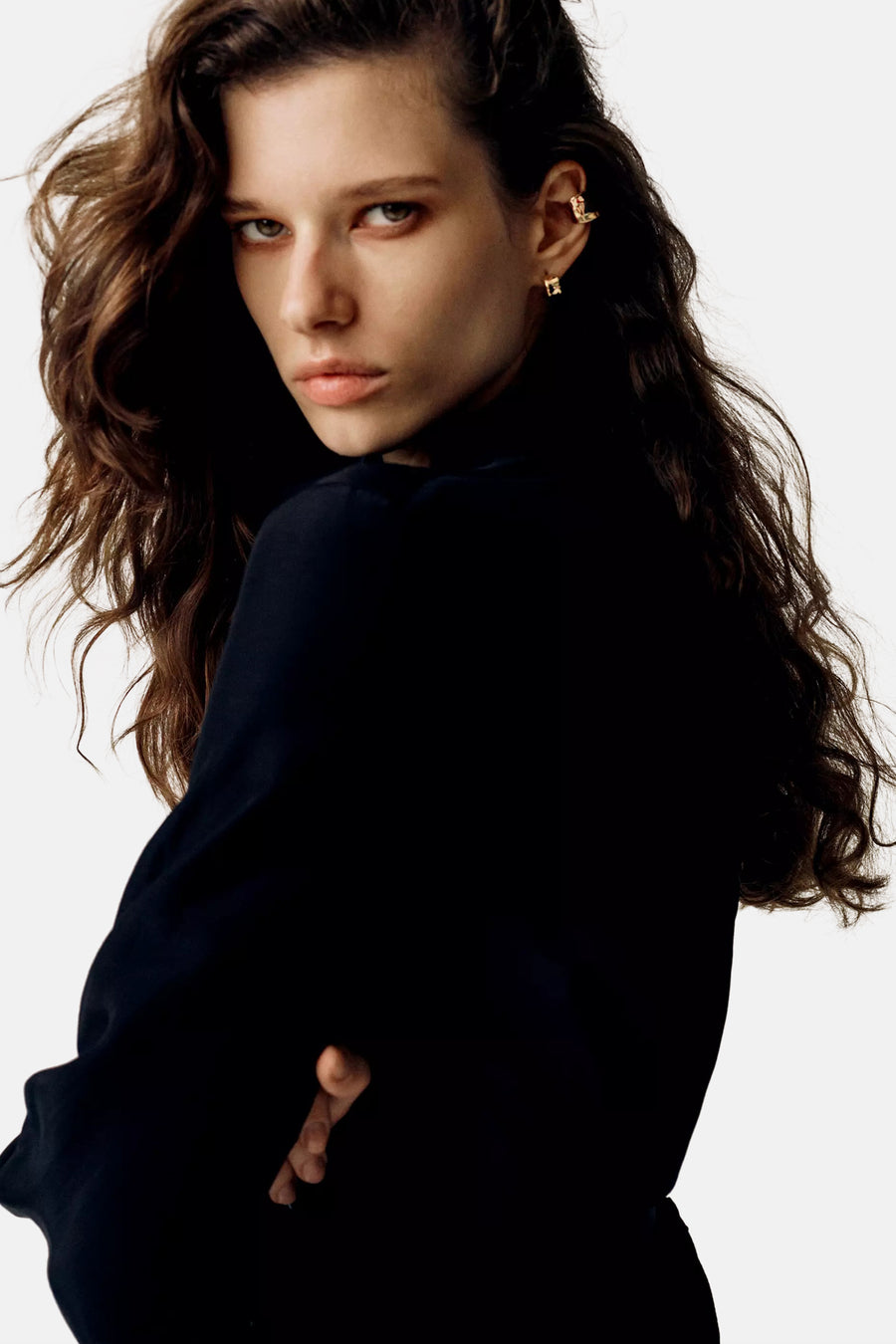 Golden stud earrings with geometric design worn by model in side profile, paired with dark top and wavy hair